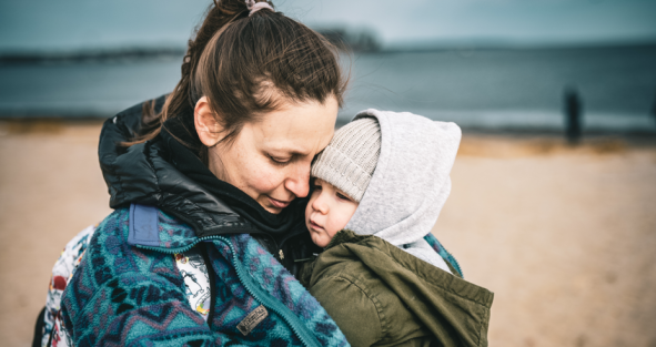 Mama knuffelt kind in haar armen, knus ingepakt in de warmte van haar jas, samen wandelend op het strand