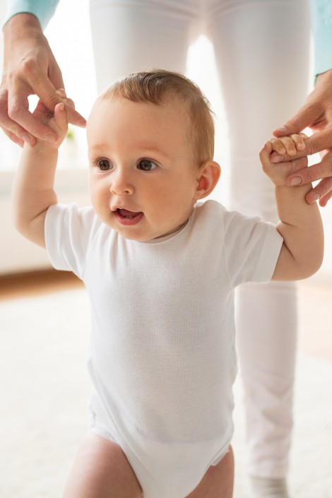 Baby leert stappen terwijl papa zijn handjes vast houdt.